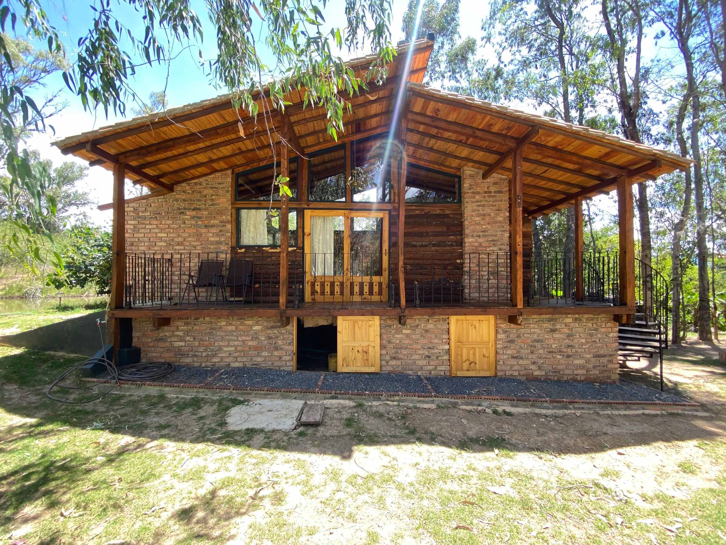 Cabaña Canto de Agua, chalet de madera sobre un zócalo de ladrillo, con terraza perimetral rodeada de árboles en Villa de Leyva