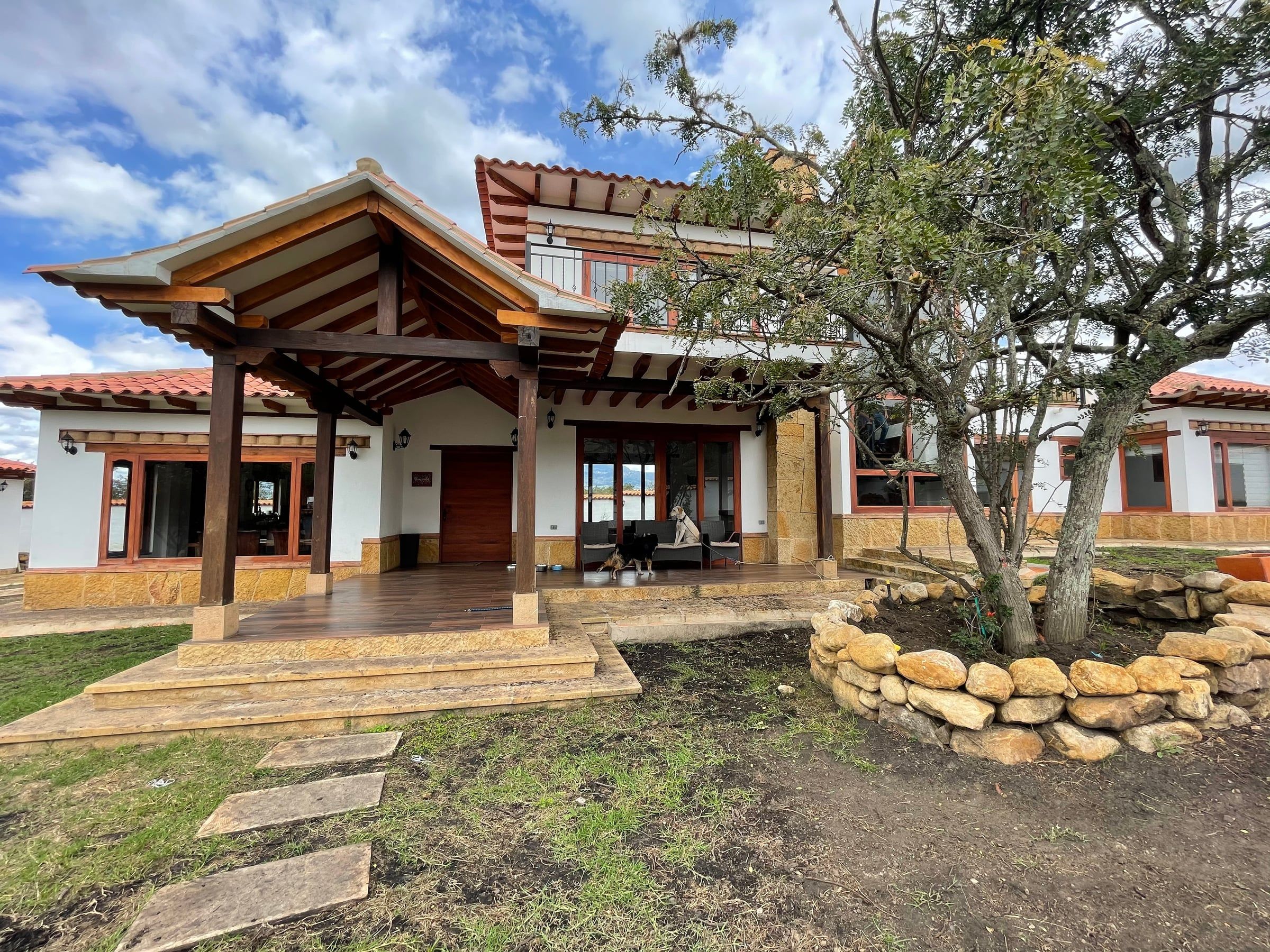 Acceso a la casa bajo una pérgola de madera, con escalones de piedra y jardín
