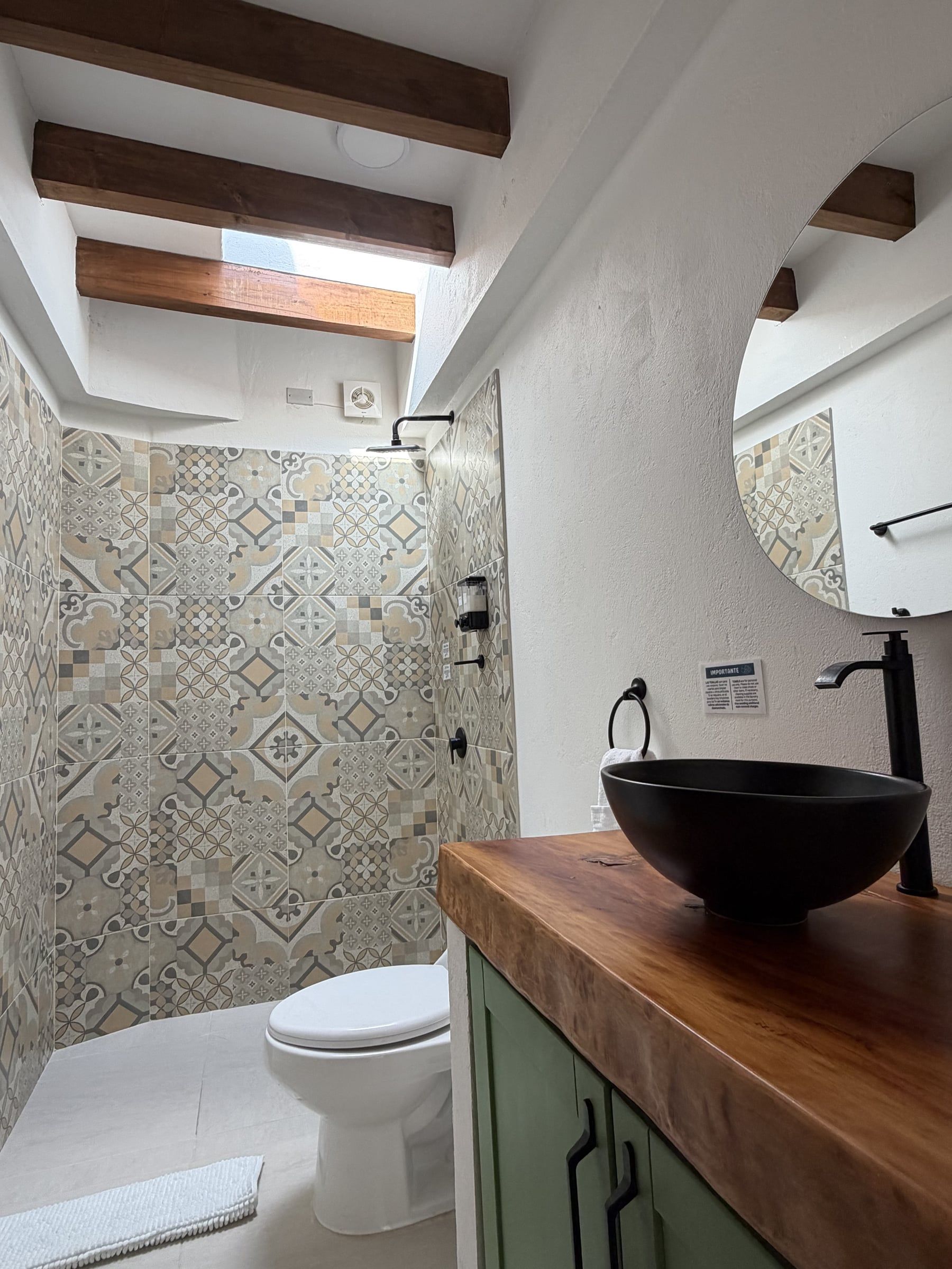 Baño con mesón de madera, lavamanos negro y baldosa decorada