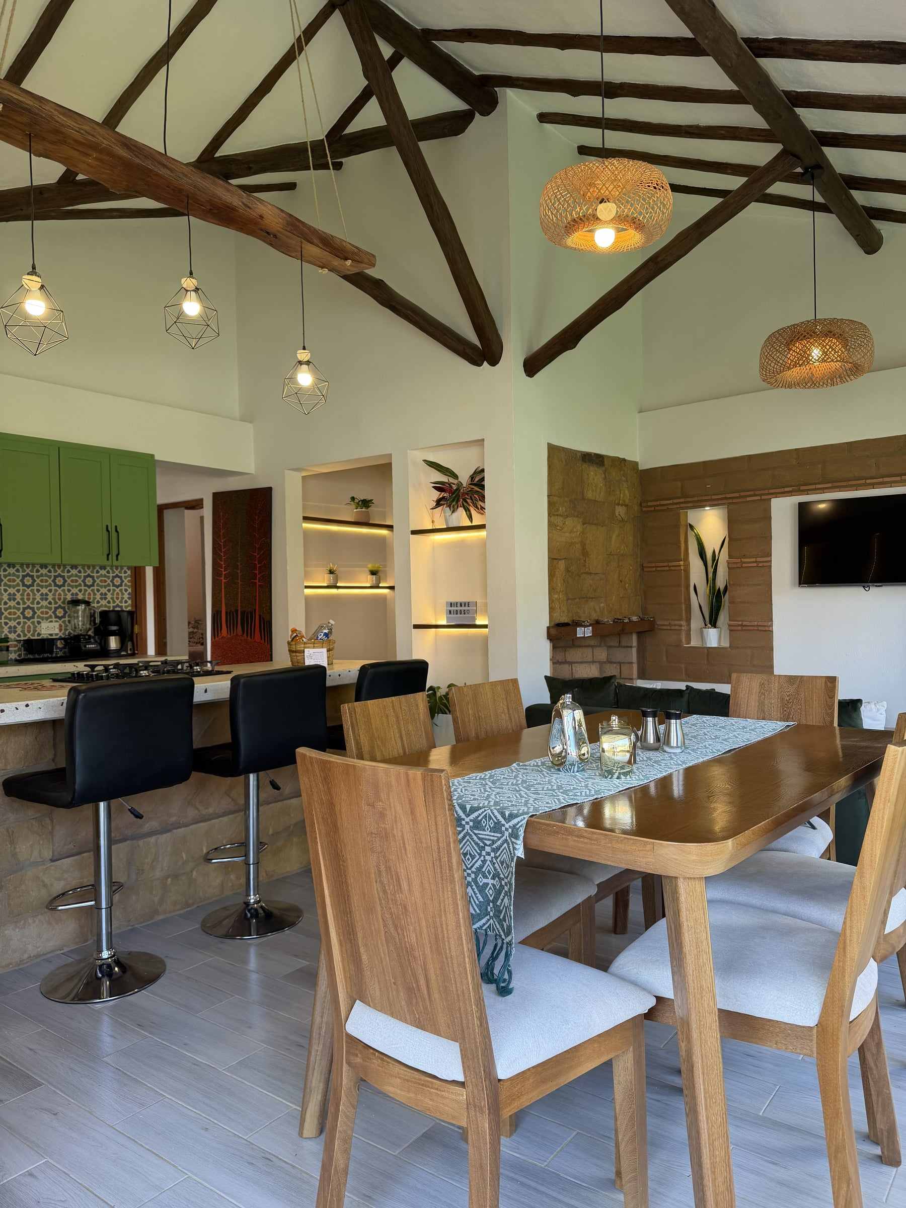 Comedor y cocina de la Casa Juan bajo una cubierta alta de vigas de madera, con lámparas de fibra natural, en el centro histórico de Villa de Leyva