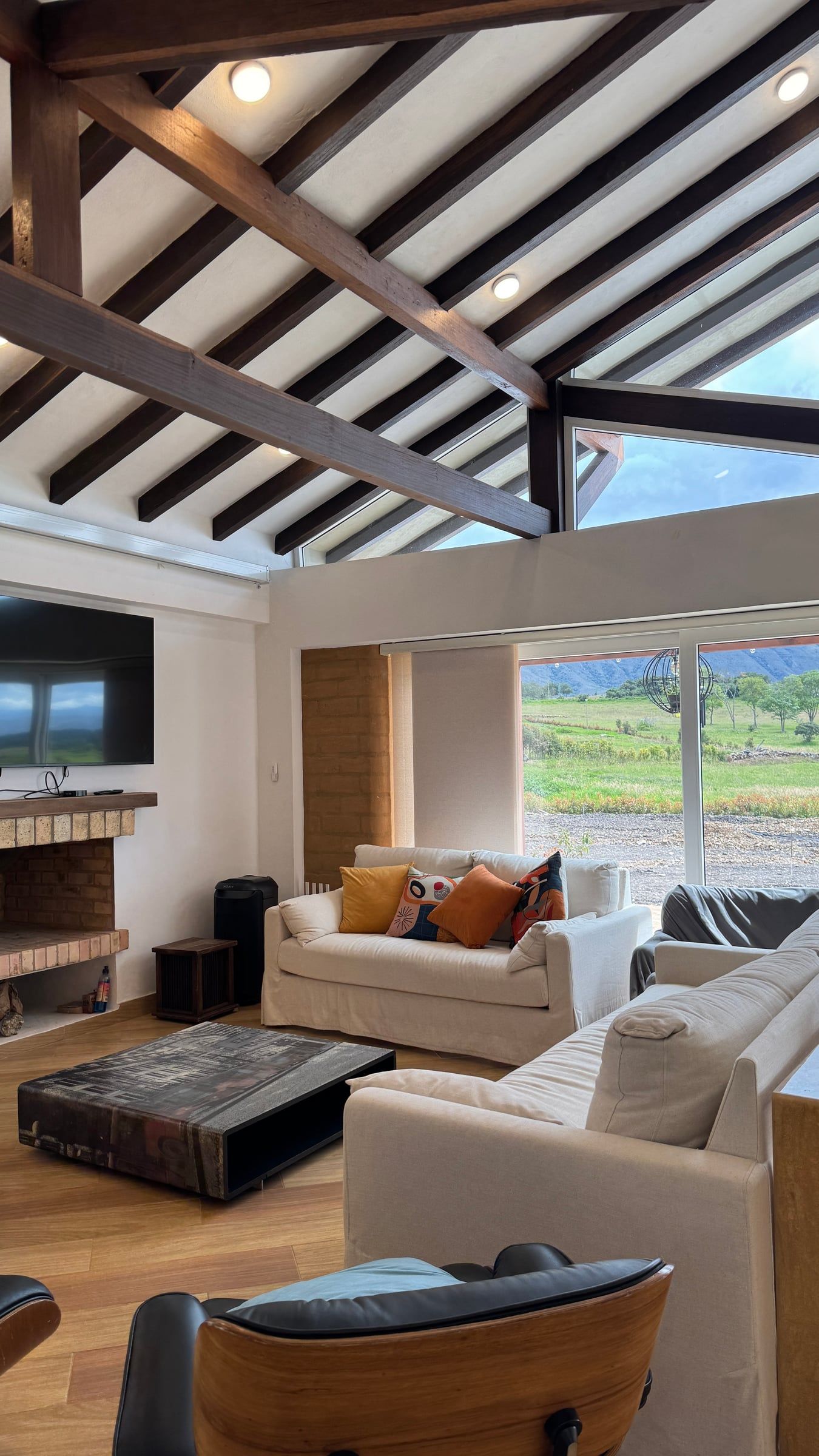 Sala con chimenea bajo la estructura de madera de la cubierta y ventanas hacia el campo