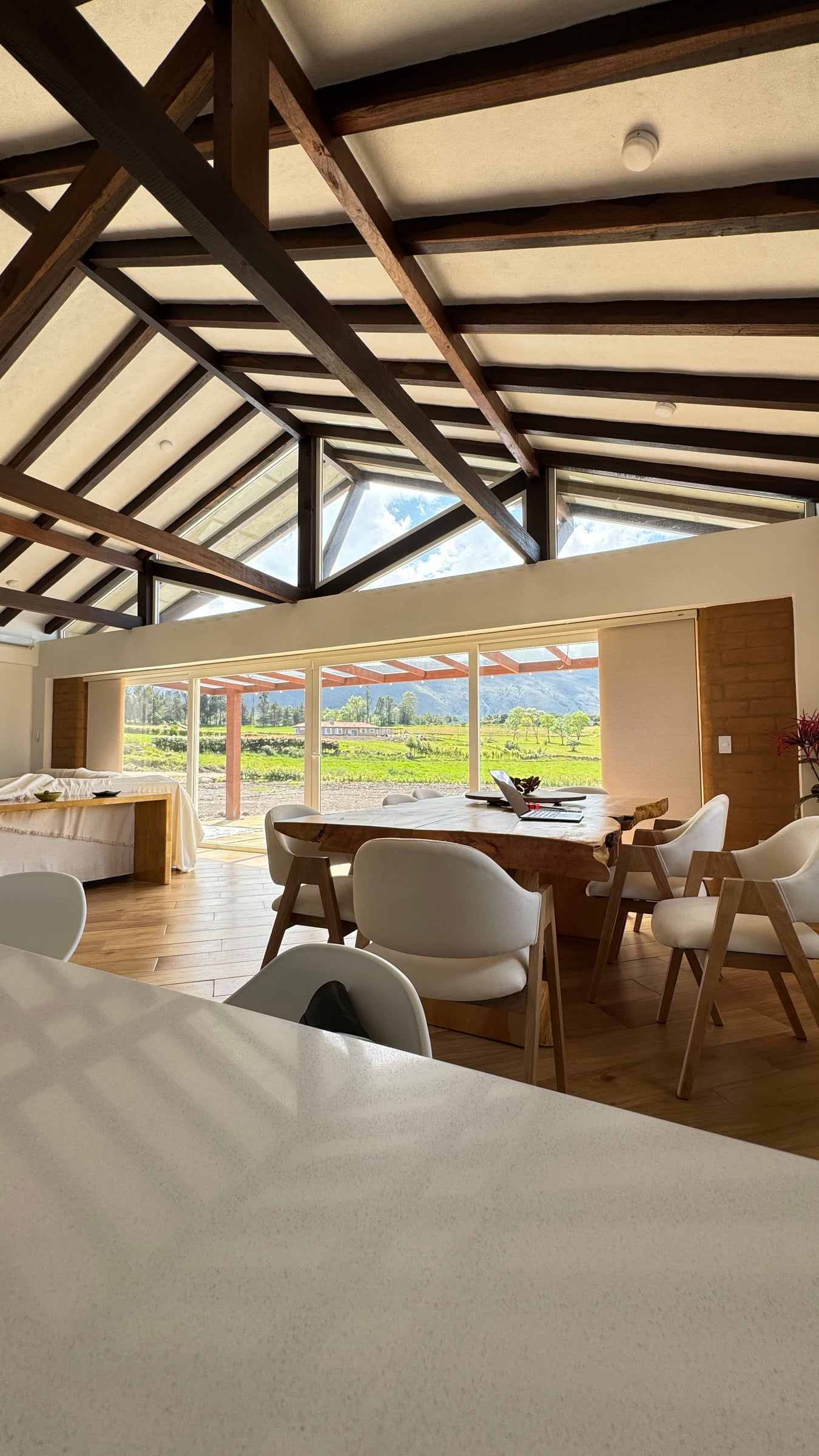 Zona social de la Casa Mariva bajo una cubierta de estructura de madera a la vista, abierta hacia el paisaje de Villa de Leyva