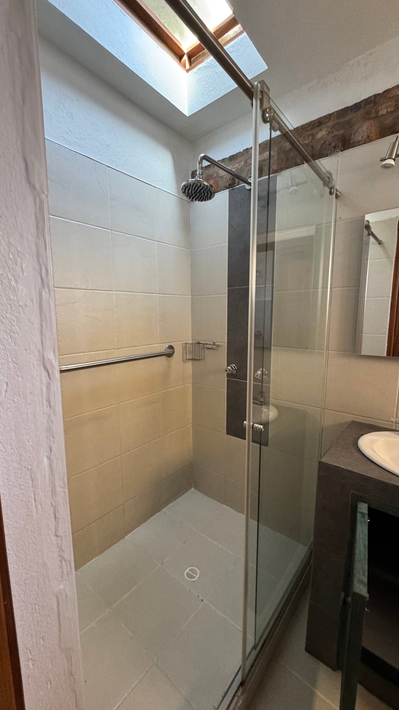 Casa Nido Verde antes de la remodelación: baño con ducha de vidrio, enchape beige y claraboya