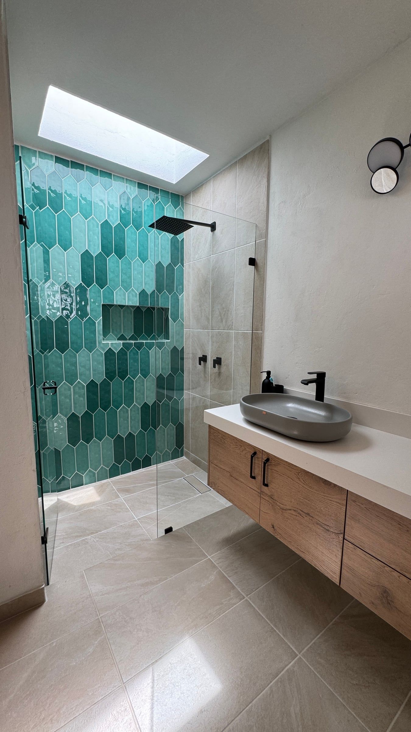 Casa Nido Verde después de la remodelación: baño con enchape verde hexagonal en la ducha, mueble de madera flotante, lavamanos de sobreponer y claraboya