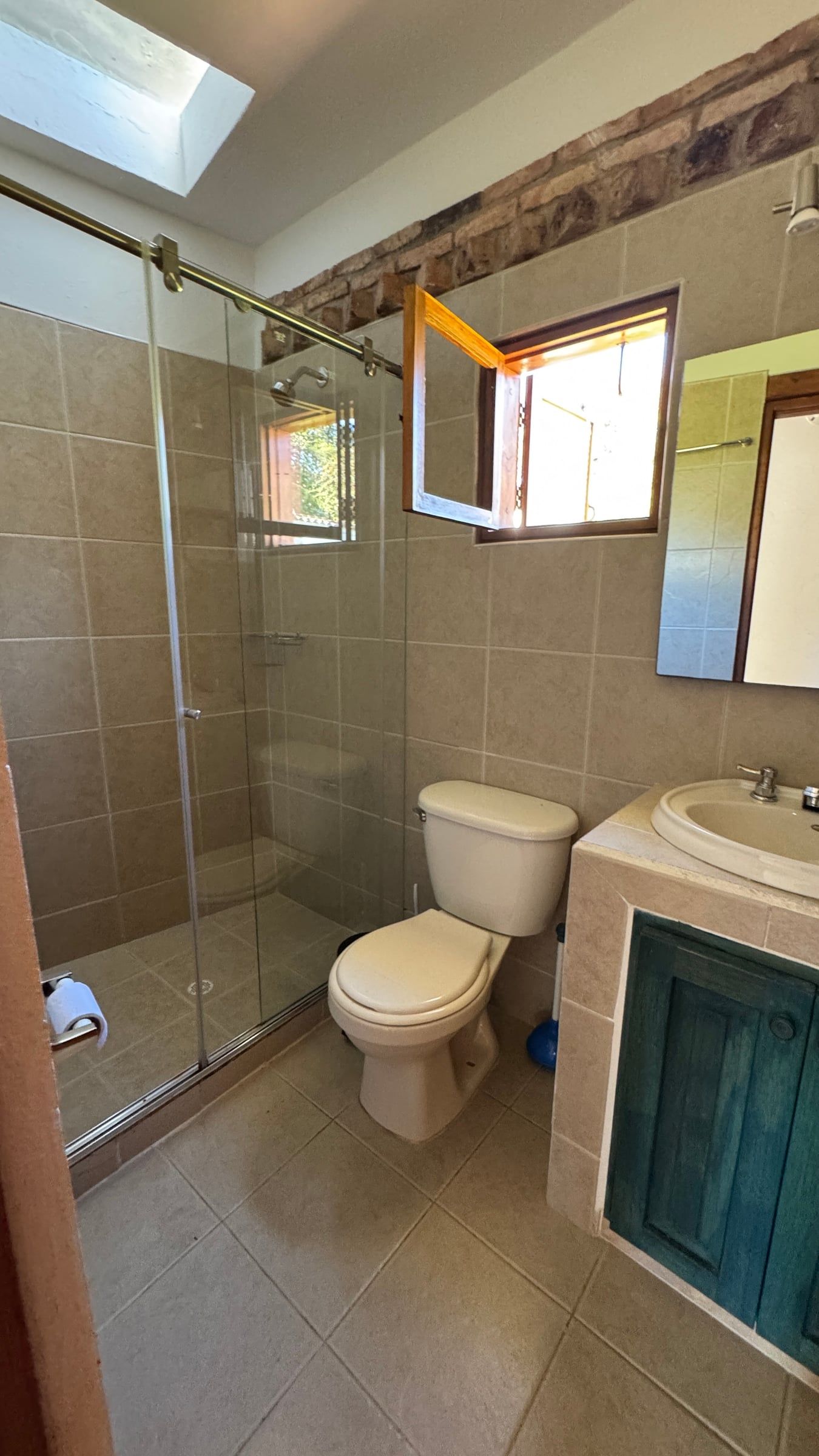 Casa Nido Verde antes de la remodelación: baño con enchape beige, mueble de obra con puerta verde y ventana de madera