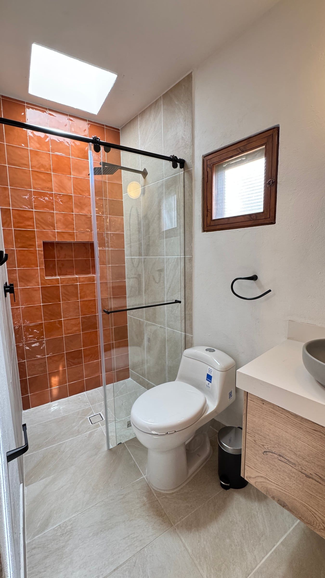 Casa Nido Verde después de la remodelación: baño con enchape terracota y nicho en la ducha, grifería negra, mueble de madera y claraboya