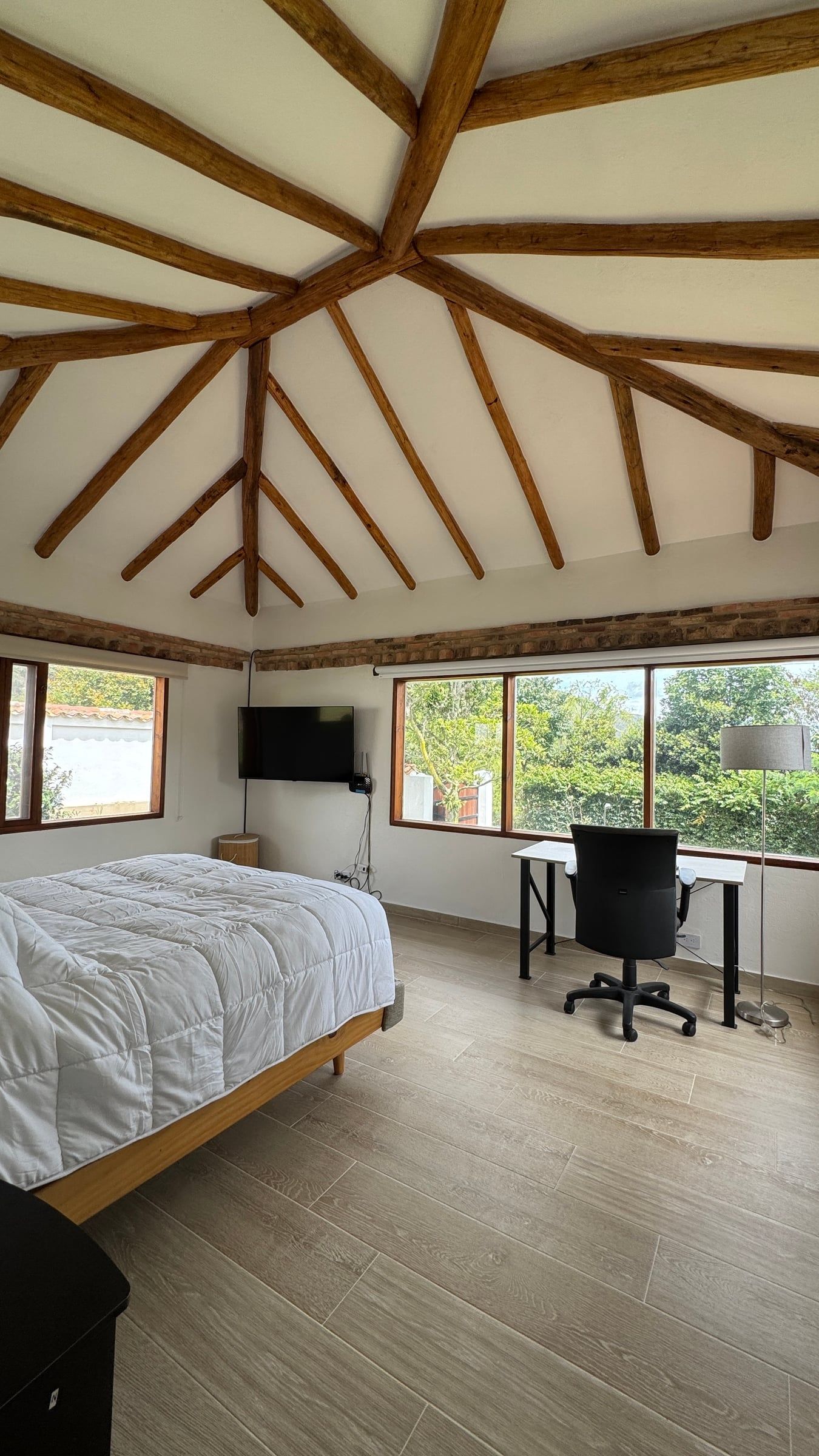 Casa Nido Verde después de la remodelación: habitación de cubierta octogonal de madera con piso claro, cama, escritorio y ventanales al jardín