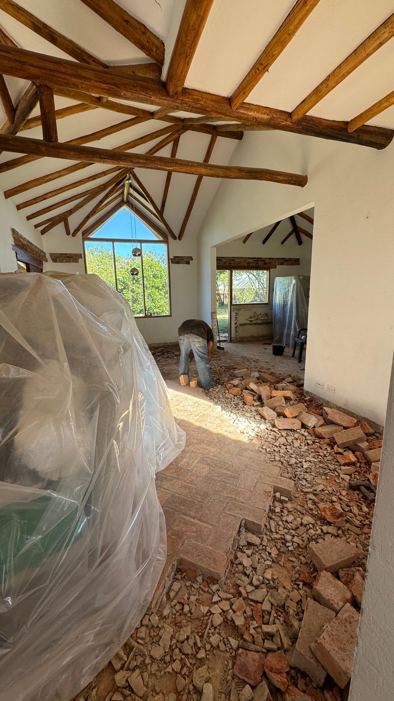 Casa Nido Verde durante la obra: sala con el piso de ladrillo levantado, muebles cubiertos y cubierta de vigas de madera con ventana en punta